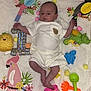 baby, infant, blanket, toy, pink_bucket, green_shovel, orange_rake, blue_octopus_toy, green_dinosaur_toy, colorful_birds, pom_poms, white_clothing, cute, child, playtime, indoors, soft_texture, portrait, lying_down, decorations
