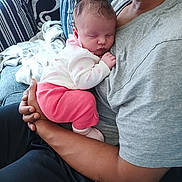 Carlina is registered to the contest to win money with this photo: baby, sleeping, infant, person, adult, couch, pillow, blanket, clothing, pink, white, gray_shirt, black_pants, hand, arm, home_interior, relaxation, indoor, comfort, rest