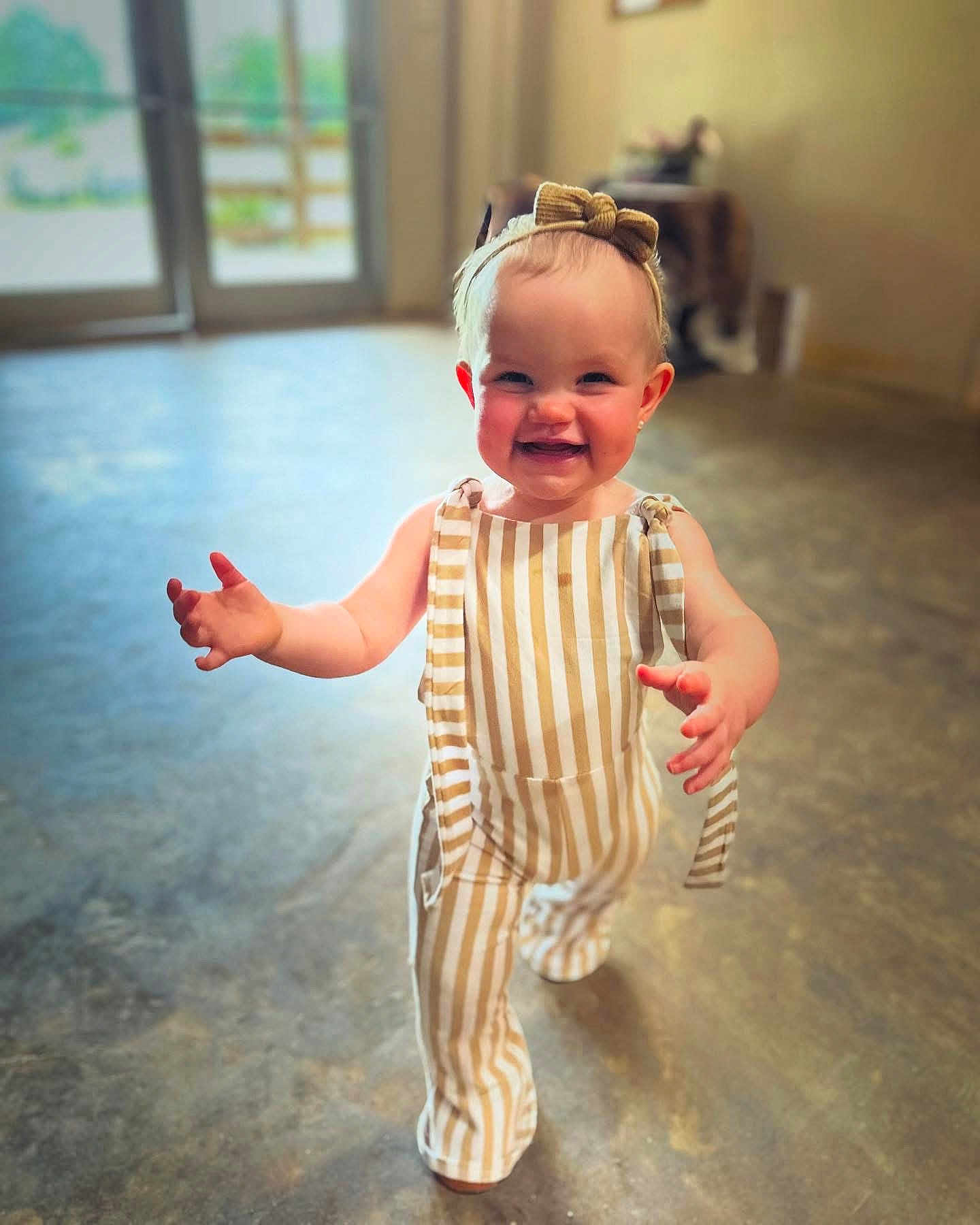 Jessie joined the competition — help win amazing prizes! toddler, child, smiling, walking, indoor, striped_overalls, headband, baby, happy, person, floor, light, shadow, blurry_background, cute, portrait, young_child, clothing, fashion, playful