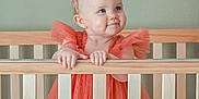 Jessie joined the competition — help win amazing prizes! baby, child, crib, party_hat, orange_dress, pom_pom, smile, cheeks, wooden_crib, infant, cute, toddler, blue_eyes, indoor, celebration, young_child, portrait, holding_crib, happy, gown