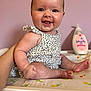 baby, smile, face, arm, hand, skin, clothing, floral_pattern, changing_pad, bottle, baby_lotion, pink_background, person, infant, sitting, happy, cute, child, indoor, support