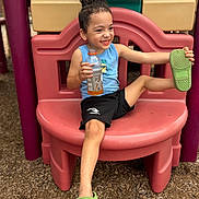 Liam joined the competition — help win amazing prizes! black_shorts, blue_shirt, child, colorful, curly_hair, green_shoes, happy, juice_bottle, outdoor, play_equipment, playful, playground, playground_slide, playground_surface, portrait, seated, shoe, sitting, smiling, summer
