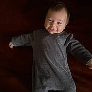 Jade participe au concours pour gagner de l'argent avec cette photo : arms_outstretched, baby, child, cozy, cute, dark_background, face, gray_clothing, happy, indoors, infant, lying_down, onesie, person, portrait, sleepwear, small, smile, soft_texture, young