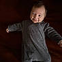 baby, infant, smile, onesie, gray_clothing, lying_down, happy, face, child, cute, portrait, arms_outstretched, dark_background, soft_texture, young, person, cozy, indoors, sleepwear, small