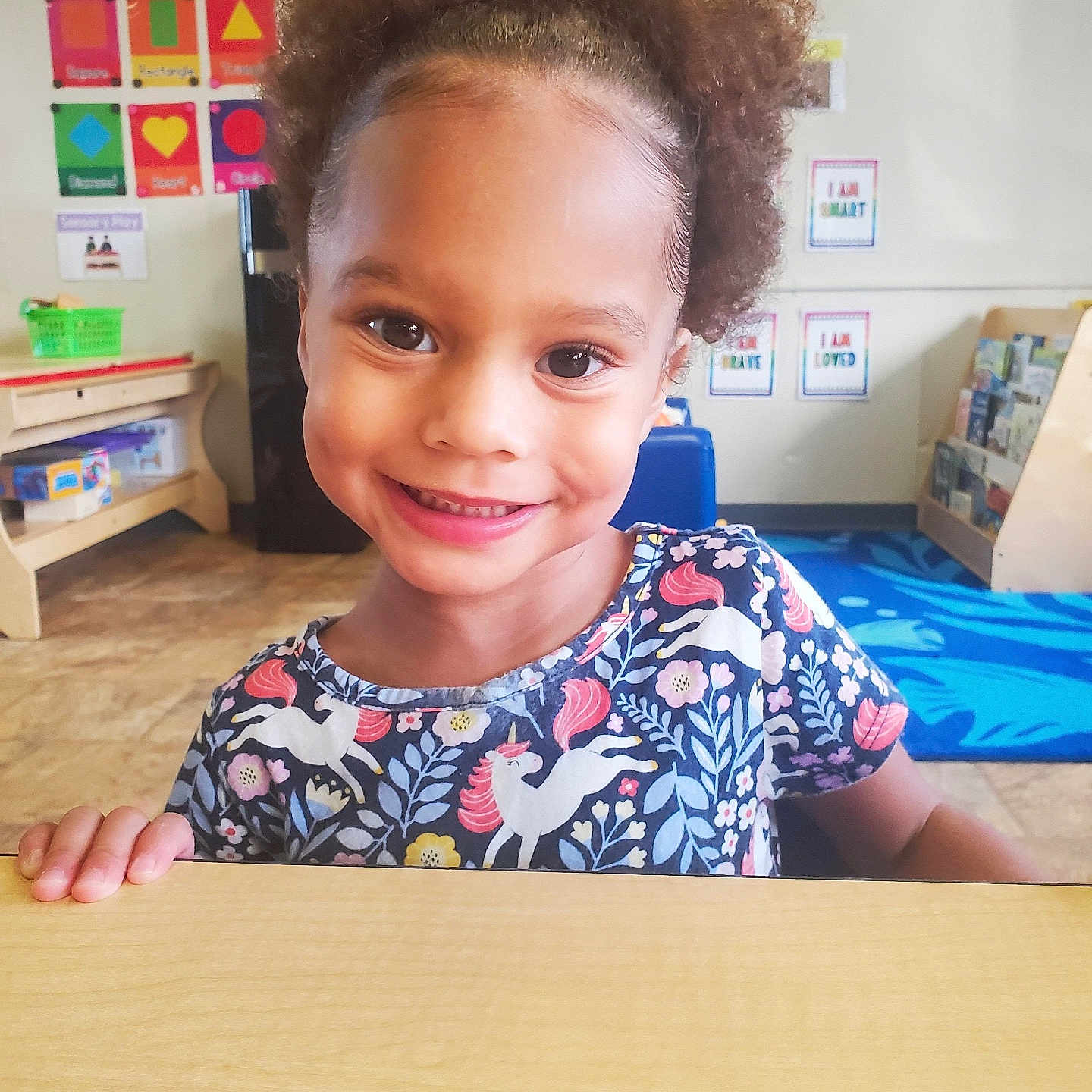 Aria joined the competition — help win amazing prizes! blue_chair, child, classroom, colorful, curly_hair, cute, educational_posters, happy, indoor, learning_environment, person, playroom, portrait, preschool, smiling, table, toys, unicorn_shirt, wooden_table, young_child