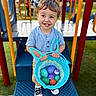 toddler, child, playground, basket, plastic_eggs, smiling, blue_shirt, shorts, sneakers, outdoor, play_equipment, colorful, happy, toy, person, daylight, grass, metal, hand, cute