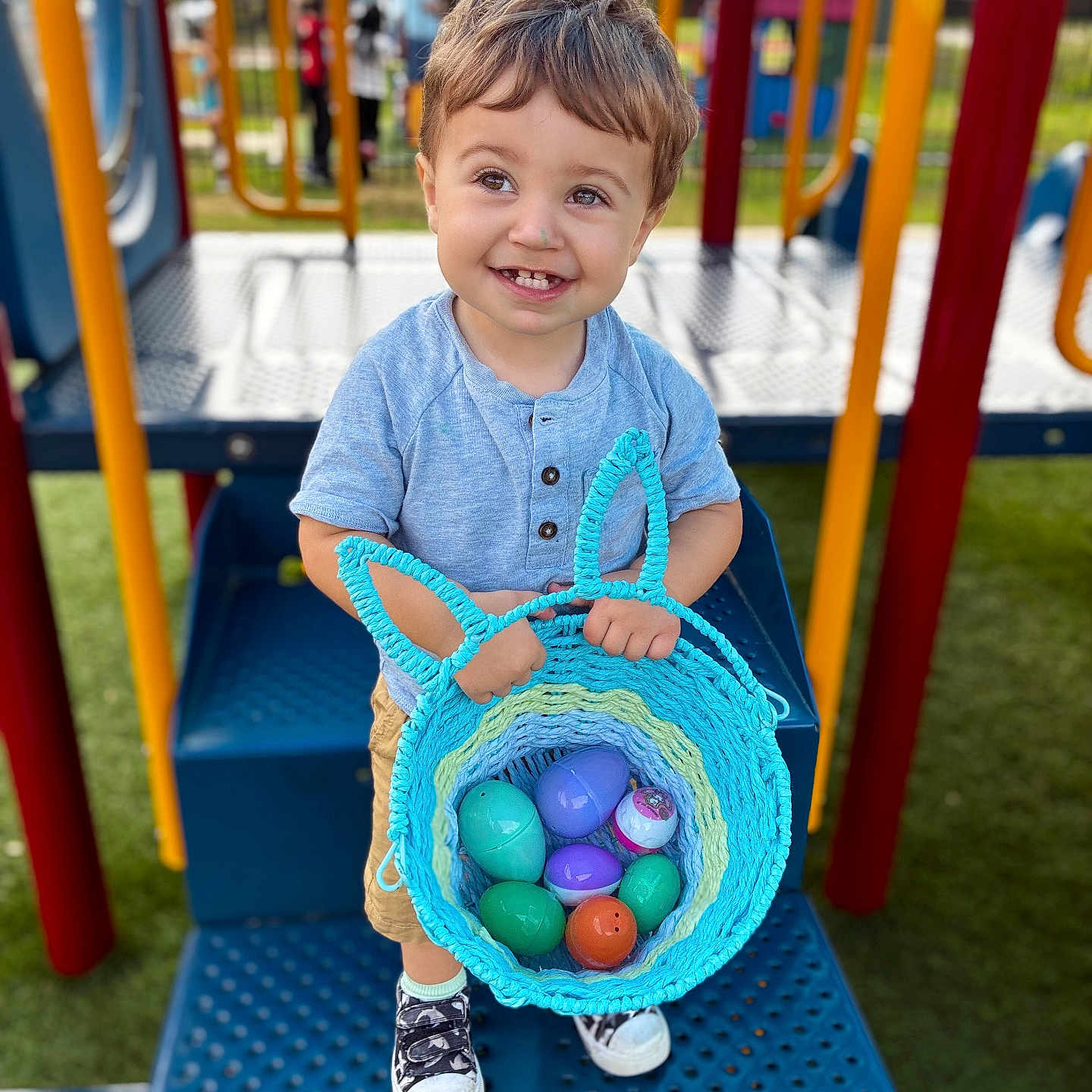 Luka joined the competition — help win amazing prizes! toddler, child, playground, basket, plastic_eggs, smiling, blue_shirt, shorts, sneakers, outdoor, play_equipment, colorful, happy, toy, person, daylight, grass, metal, hand, cute