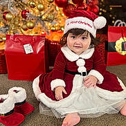 Adhara is registered to the contest to win money with this photo: toddler, child, christmas, holiday, santa_hat, red_dress, festive_clothing, gift_bags, christmas_tree, ornaments, carpet, indoor, celebration, holiday_decorations, cute, smiling, portrait, festive_boots, holiday_spirit, seasonal