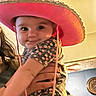 baby, infant, child, portrait, cowboy_hat, pink_hat, floral_outfit, held, adult_hands, wide_eyes, face, indoor, warm_lighting, close_up, smiling, cute, fashion, adorable, photograph, family