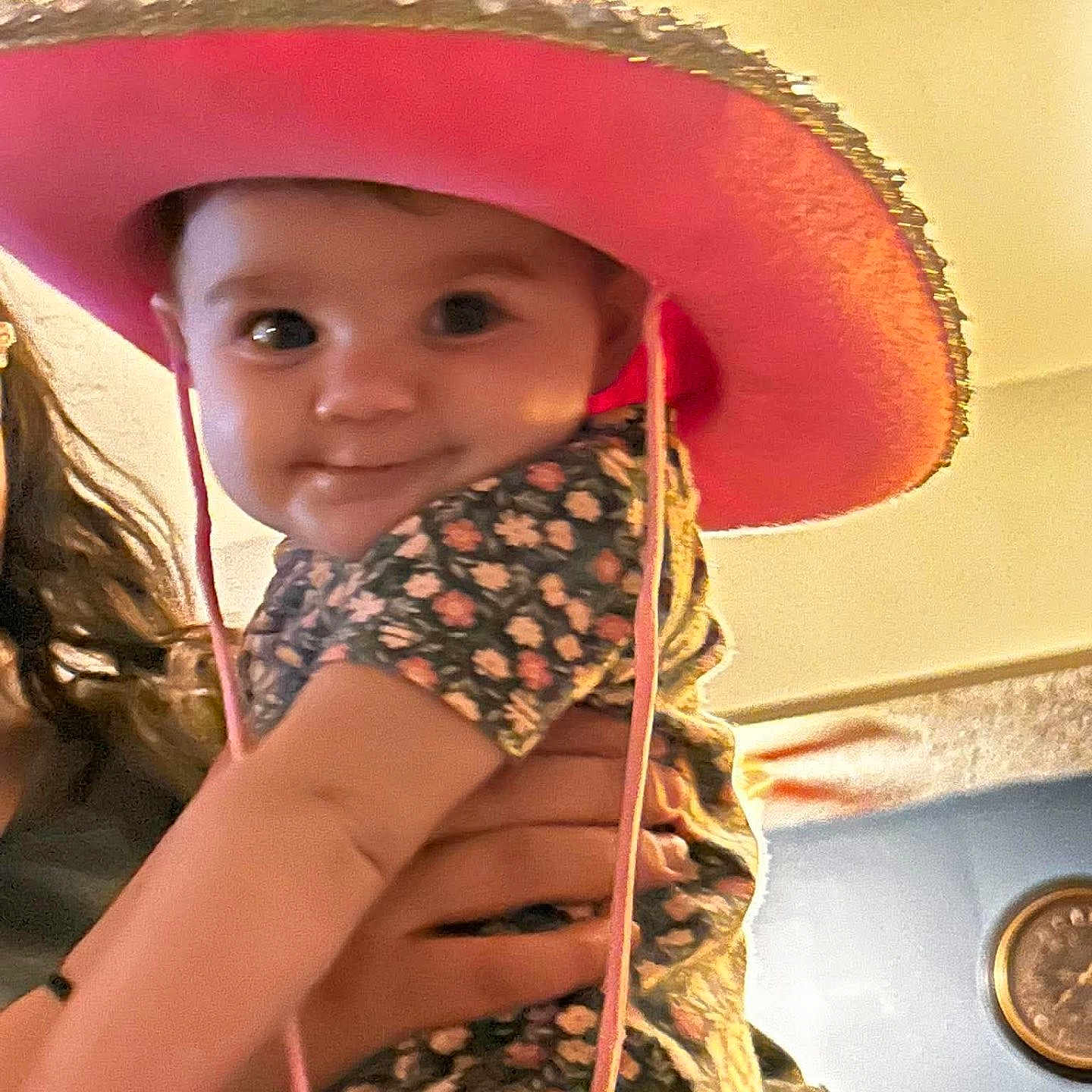 Wrenlee is registered to the contest to win money with this photo: baby, infant, child, portrait, cowboy_hat, pink_hat, floral_outfit, held, adult_hands, wide_eyes, face, indoor, warm_lighting, close_up, smiling, cute, fashion, adorable, photograph, family