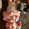 baby, infant, child, portrait, upside_down, couch, cat, stuffed_animal, toy, bottle, onesie, pink_clothing, hands, feet, smiling, indoors, living_room, furniture, pet, playful