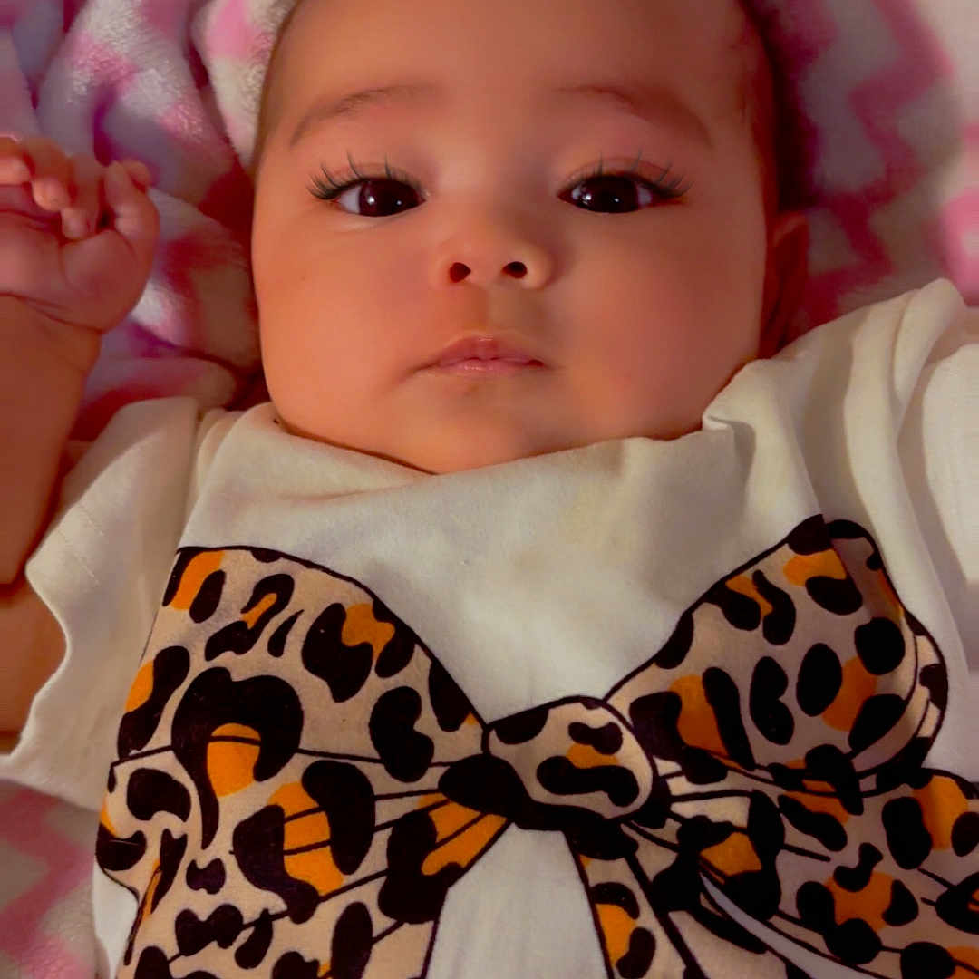 Aaliyah joined the competition — help win amazing prizes! baby, infant, face, eyes, clothing, shirt, bow, pattern, leopard_print, blanket, pink, white, chevron, hand, soft, lying_down, portrait, cute, child, indoors