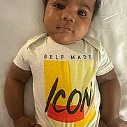 Jayceon is registered to the contest to win money with this photo: baby, infant, child, onesie, clothing, text_on_clothing, face, arms, legs, skin, lying_down, blanket, indoors, portrait, cute, young, expression, closeup, person, toddler