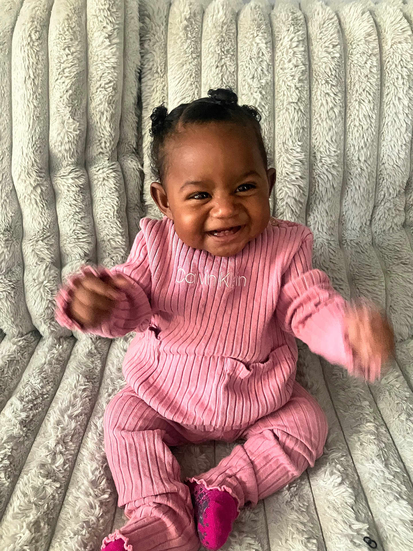 Akiyra is registered to the contest to win money with this photo: baby, child, smiling, pink_clothing, ribbed_outfit, happy, sitting, fuzzy_blanket, cozy, indoors, cute, infant, portrait, baby_girl, face, hair_buns, sock, texture, soft, celebration