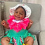 Akiyra joined the competition — help win amazing prizes! baby, chair, colorful, cushion, cute, decorative_flowers, flower_lei, footwear, green_skirt, happy, hat, indoor, infant, person, portrait, skin, smiling, striped_clothing, toddler, tropical