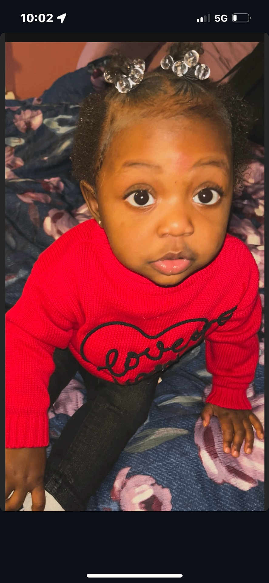 Kinzey is registered to the contest to win money with this photo: toddler, child, red_sweater, heart_design, curly_hair, hair_accessories, big_eyes, floral_blanket, indoor, portrait, cute, sitting, hand, clothing, young_child, person, cozy, warm_clothes, closeup, expression