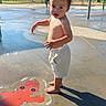 Ronan joined the competition — help win amazing prizes! child, toddler, boy, outdoor, splash_pad, water, playground, barefoot, shorts, shirtless, standing, portrait, face, curious, sunlight, shadow, wet_pavement, octopus, playground_equipment, summer