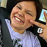 child, smiling, portrait, selfie, car, car_seat, seat_belt, indoors, vehicle, happy, teeth, face, dark_hair, purple_shirt, hand_gesture, ring, bracelet, window, daylight, playful