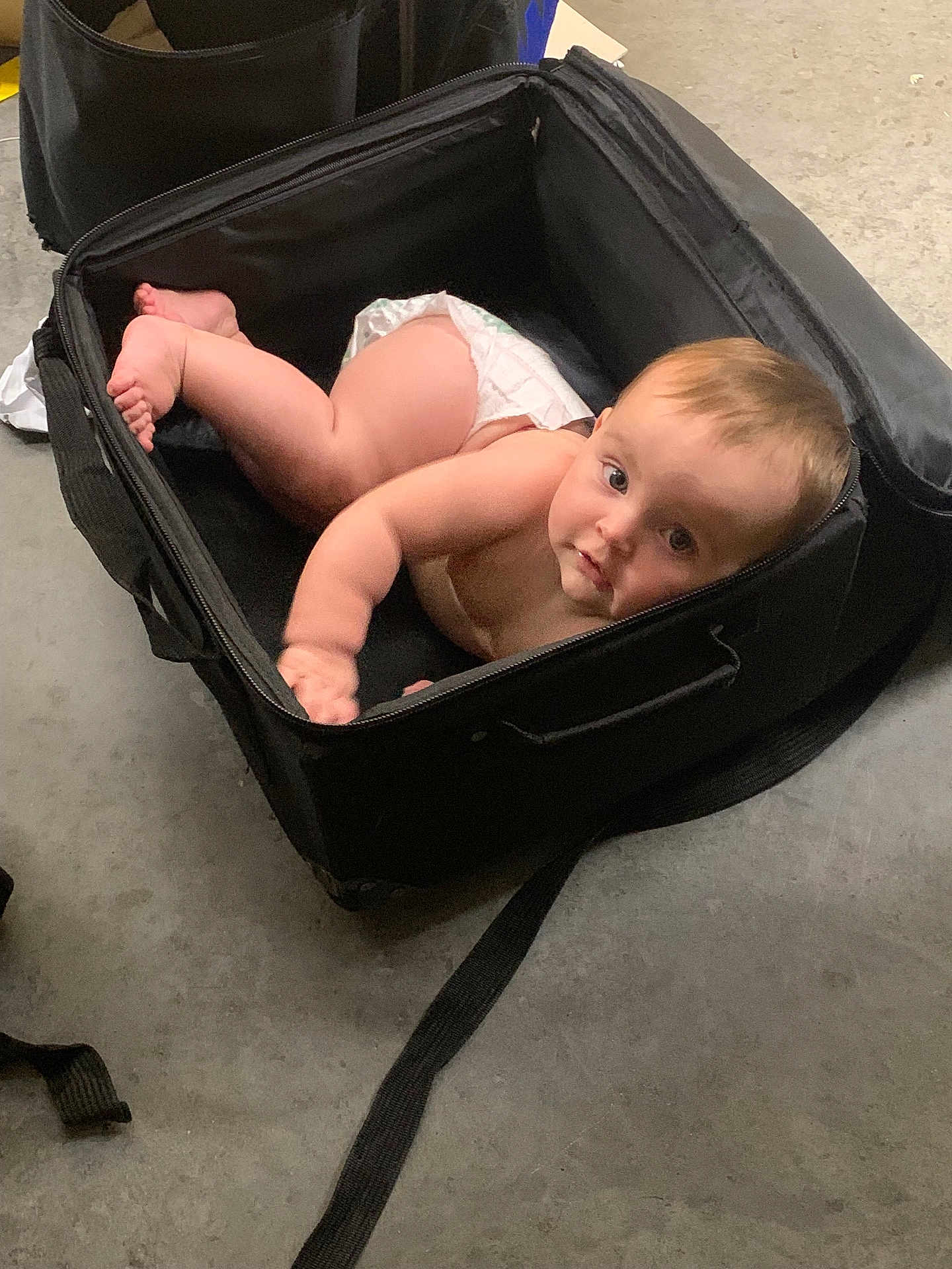 Isabella joined the competition — help win amazing prizes! baby, diaper, suitcase, floor, curious, infant, looking_up, black, open, concrete, indoor, child, person, young, crawling, cute, small, playful, expression, container