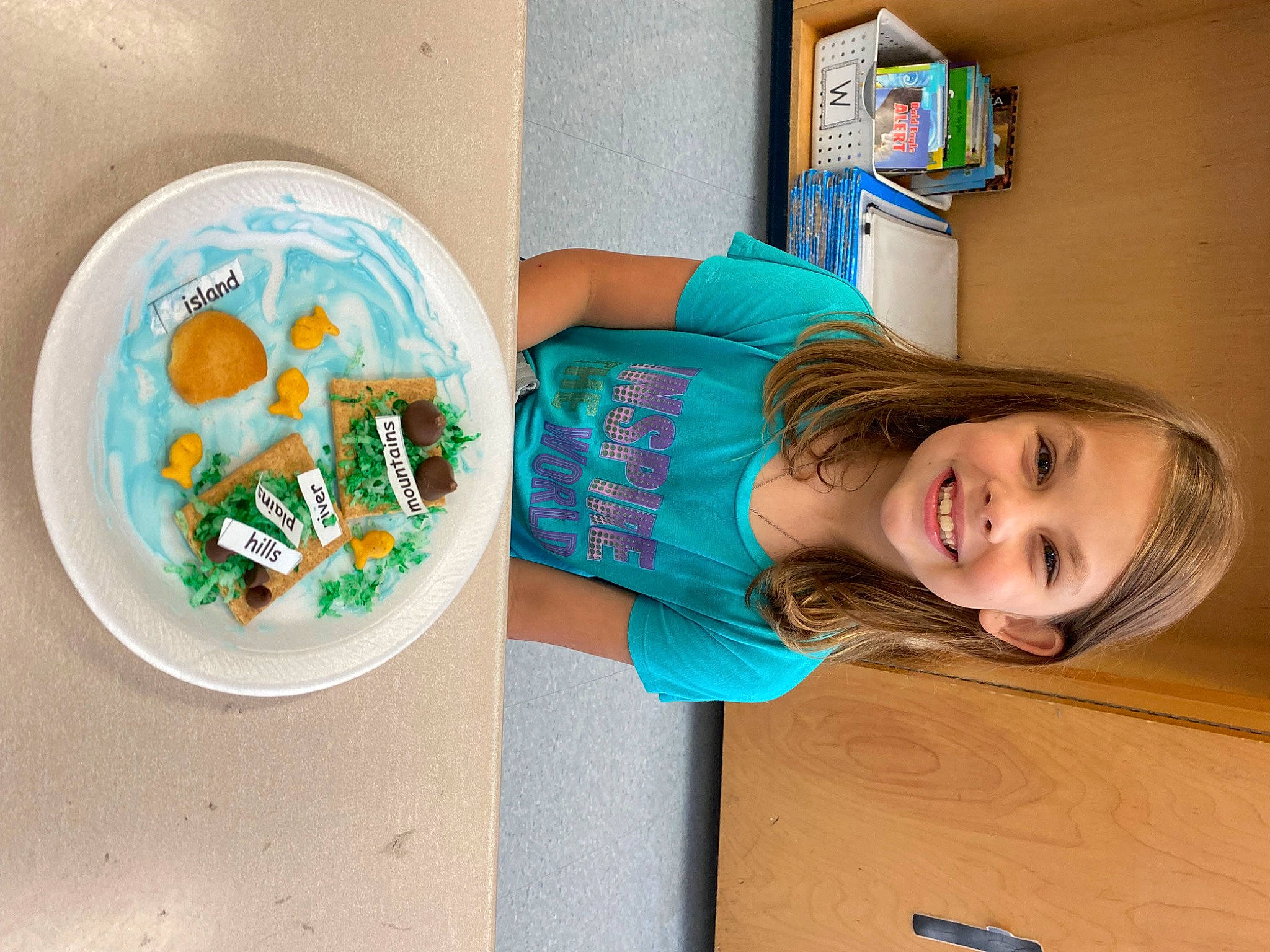 Ava-grace is registered to the contest to win money with this photo: chair, child, comfort_food, dishware, food, fun, happy, joy, leisure, person, plastic, plate, play, room, shelf, shelving, smile, t_shirt, table, toddler