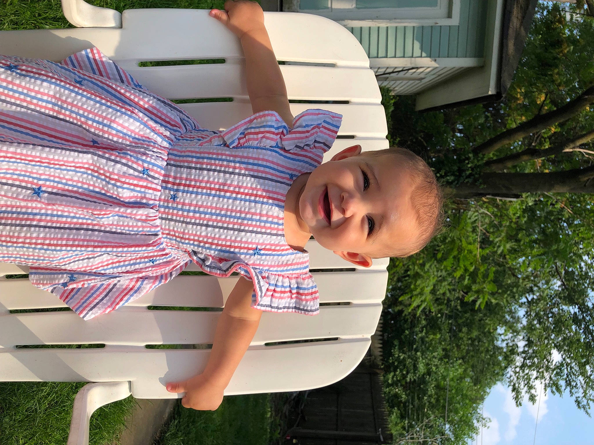 Melani is registered to the contest to win money with this photo: child, facial_expression, fun, grass, green, happy, human_leg, joy, leisure, pattern, person, plaid, plant, public_space, shoulder, sitting, sky, tartan, thigh, toddler