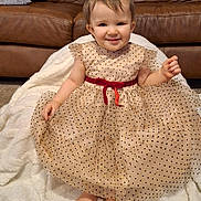 Charlee-Jo is registered to the contest to win money with this photo: child, toddler, baby, polka_dot_dress, red_belt, barefoot, smile, face, sitting, white_blanket, leather_sofa, living_room, carpet, toes, portrait, cute, hair, pillow, cozy, adorable