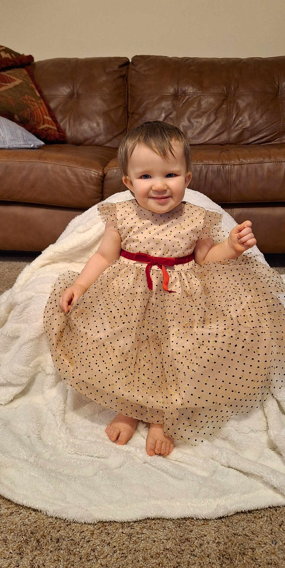 Charlee-Jo is registered to the contest to win money with this photo: child, toddler, baby, polka_dot_dress, red_belt, barefoot, smile, face, sitting, white_blanket, leather_sofa, living_room, carpet, toes, portrait, cute, hair, pillow, cozy, adorable