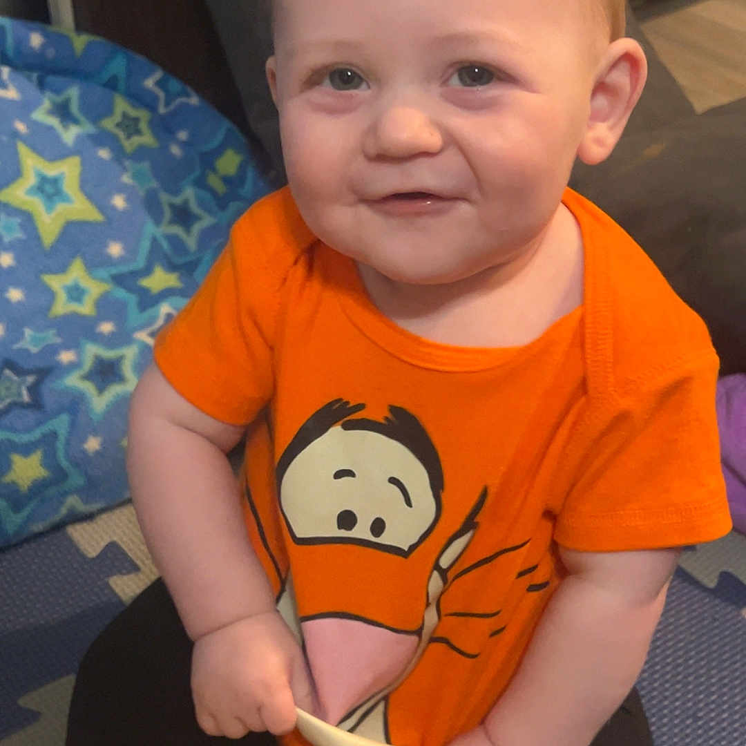Xander joined the competition — help win amazing prizes! baby, blanket, cartoon_print, child, clothing, cute, face, floor, hand, happy, head, indoor, orange_shirt, person, play_mat, plush_toy, sitting, smiling, toddler, toy