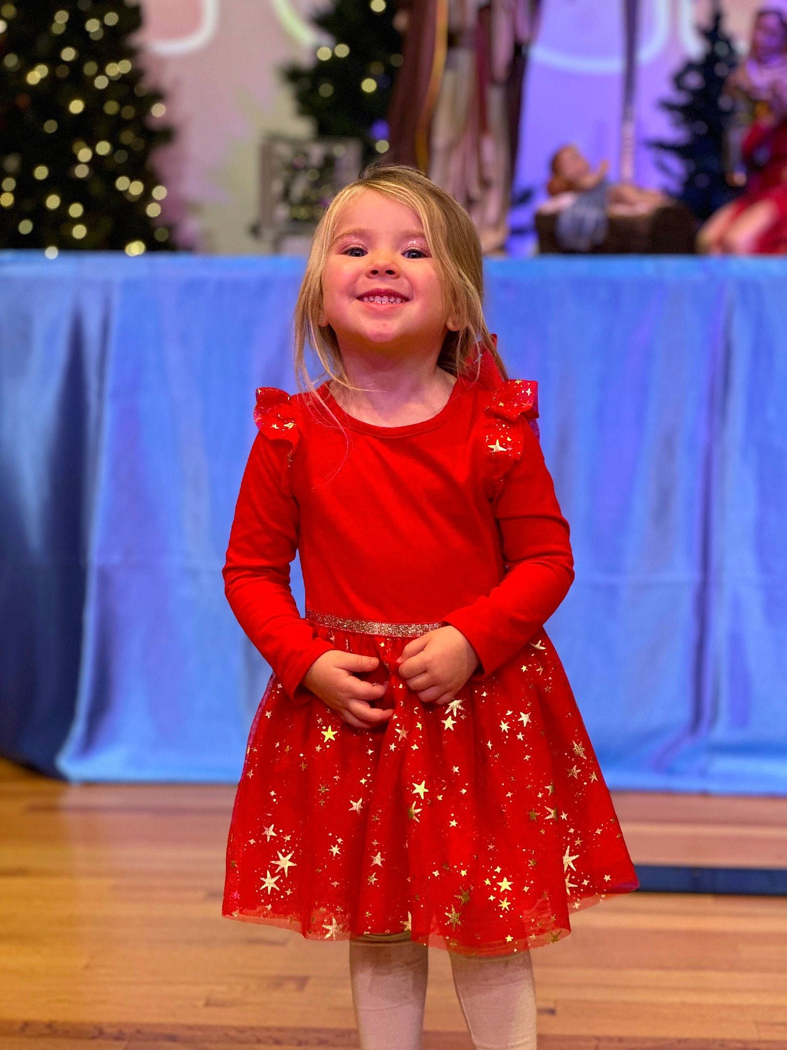 Piper is registered to the contest to win money with this photo: child, christmas_tree, dress, electric_blue, entertainment, event, fashion_design, flooring, formal_wear, fun, happy, hardwood, joy, lighting, performance_art, performing_arts, person, smile, standing, toddler