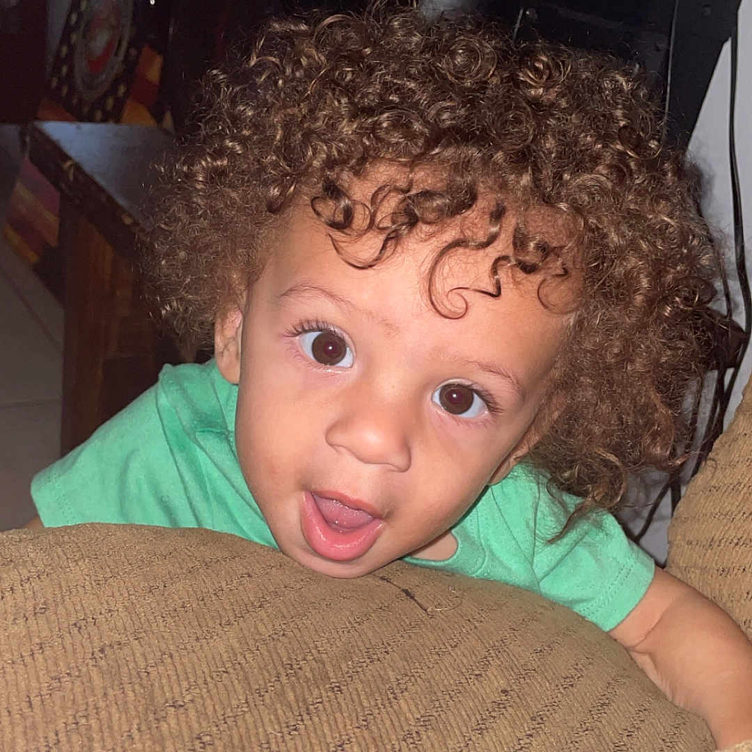 Camari joined the competition — help win amazing prizes! brown, child, couch, curious, curly_hair, cushion, expression, face, furniture, green_shirt, hair, indoor, living_room, open_mouth, person, skin, smiling, toddler, wide_eyes, young