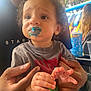 Camari is registered to the contest to win money with this photo: child, toddler, adult_hands, face, blue_frosting, curly_hair, gray_shirt, outdoor, daylight, background_people, inflatable, cup, table, person, smudged_face, expression, holding, hands, close_up, casual_clothing