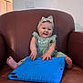 baby, child, headband, green_dress, tablet_case, blue, brown_chair, leather, smiling, happy, sitting, indoors, cute, hands, feet, wall, light_switch, portrait, playful, young_child