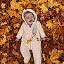 baby, child, autumn, fall_leaves, leaves, outdoor, onesie, hooded_clothing, smiling, cute, infant, lying_down, seasonal, nature, playful, warm_clothing, person, forest_floor, happy, winnie_the_pooh