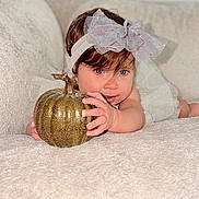 Aisha is registered to the contest to win money with this photo: baby, child, infant, portrait, smiling, autumn, pumpkin, golden_pumpkin, bow, headband, brown_hair, blue_eyes, crawling, sitting, blanket, bed, indoors, cozy, seasonal, cute