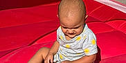 Gian is registered to the contest to win money with this photo: toddler, child, inflatable, play_area, red, sunlight, shadow, hand, sitting, outdoor, yellow, grey_outfit, pattern, baby, expression, summer, cute, person, playtime, young