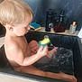 toddler, child, sink, water, bath, sponge, kitchen, faucet, soap_dispenser, playing, wet_skin, bath_time, sitting, splashing, blond_hair, candid, indoor, young_child, cleaning, fun