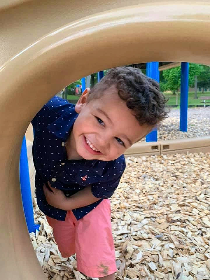 Johnathon is registered to the contest to win money with this photo: baby_toddler_clothing, child, city, clothing, eye, fun, grass, happy, joy, leisure, outdoor_play_equipment, people_in_nature, person, plant, playground, playground_slide, recreation, sitting, skin, smile