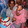 balloon, birthday_cake, cake, celebration, child, colorful, decorations, festive, hair_bows, happy, holding, indoor, party, person, pink_dress, princess_theme, smile, table, tutu, woman