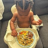 baby, braided_hair, child, couch, diaper, eating, feeding, food, gray_furniture, high_chair, indoor, ketchup, meal, messy, person, plate, sausage, scrambled_eggs, tableware, toddler