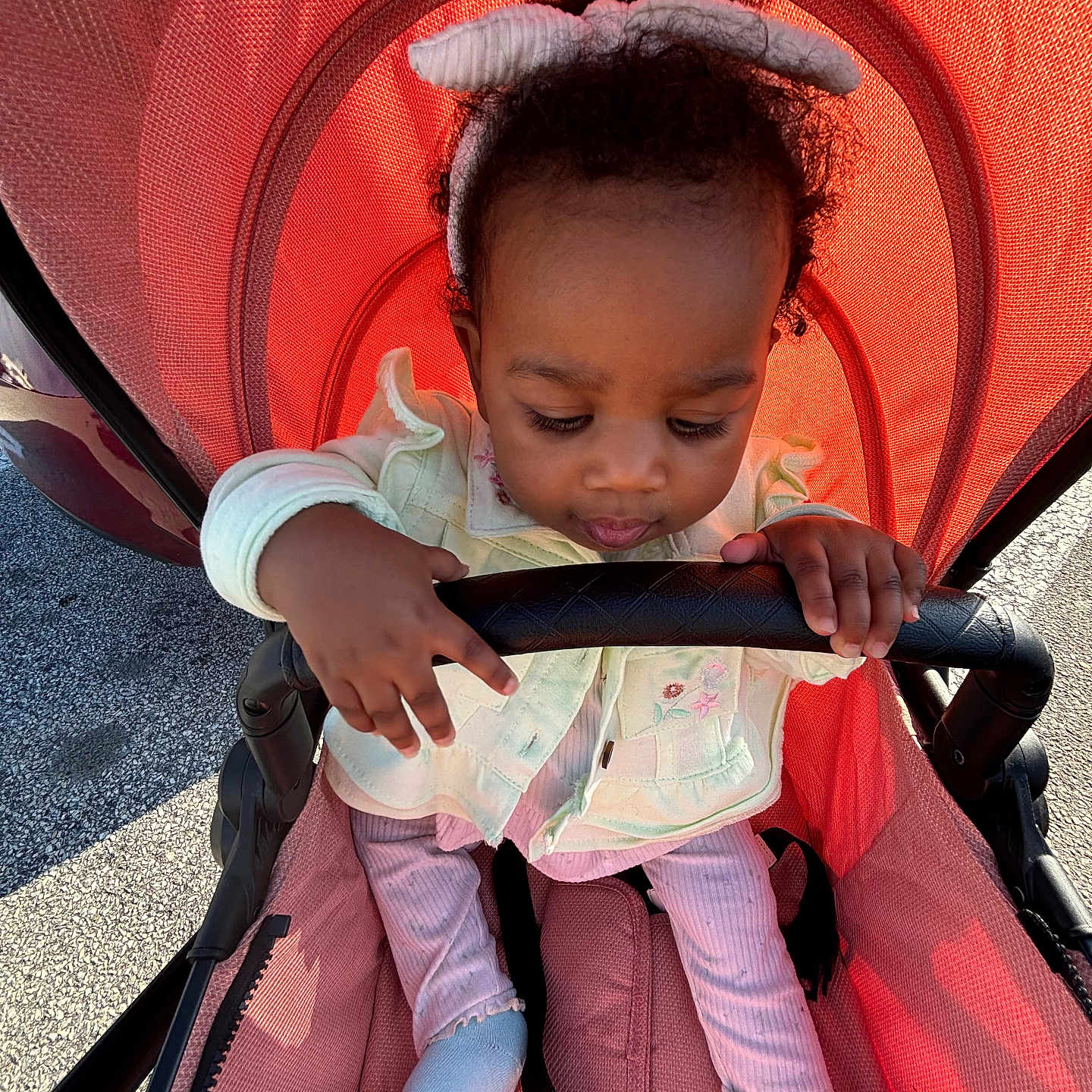 Nyuri is registered to the contest to win money with this photo: baby, child, clothing, curly_hair, fabric, grip, hand, headband, jacket, outdoor, pastel_colors, pink_pants, portrait, red_stroller, seat_belt, shadow, socks, stroller, sunlight, toddler