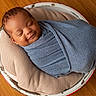 baby, sleeping, wrapped, blanket, blue, cushion, beige, bucket, wooden_floor, infant, peaceful, cozy, portrait, indoor, newborn, smiling, child, head, face, resting