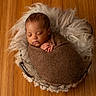 Kyrie is registered to the contest to win money with this photo: newborn, baby, sleeping, wrapped, blanket, basket, fur, wooden_floor, cozy, soft_lighting, peaceful, infant, portrait, indoors, cute, resting, child, tender, warm_colors, knitted