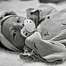 baby, black_and_white, blanket, bow_headband, close_up, cozy, eyes, face, floral_pattern, hand, hat, infant, lying_down, newborn, onesie, pacifier, portrait, sleepwear, soft_texture, striped_clothing