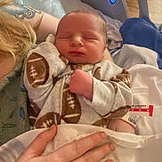 Braxton is registered to the contest to win money with this photo: newborn, baby, sleeping, infant, pajamas, football_pattern, tattoo, hand, hospital, blanket, bed, person, closeup, cozy, resting, skin, comfort, indoor, parent, care