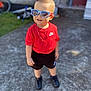 toddler, child, boy, sunglasses, mohawk, red_shirt, nike, shorts, necklace, cross, outdoor, concrete, footwear, black_shoes, standing, sunny, bicycle, background_blur, casual, portrait
