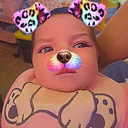 Aurora is registered to the contest to win money with this photo: baby, infant, face_filter, dog_filter, rainbow_colors, bib, pink_clothing, indoors, living_room, television, furniture, cartoon_design, cute, child, portrait, person, closeup, head, eyes, expression