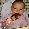 baby, child, high_chair, spatula, chocolate, face, messy, pink_clothing, stars, indoor, cute, smile, eating, happy, infant, person, toddler, closeup, hand, cooking
