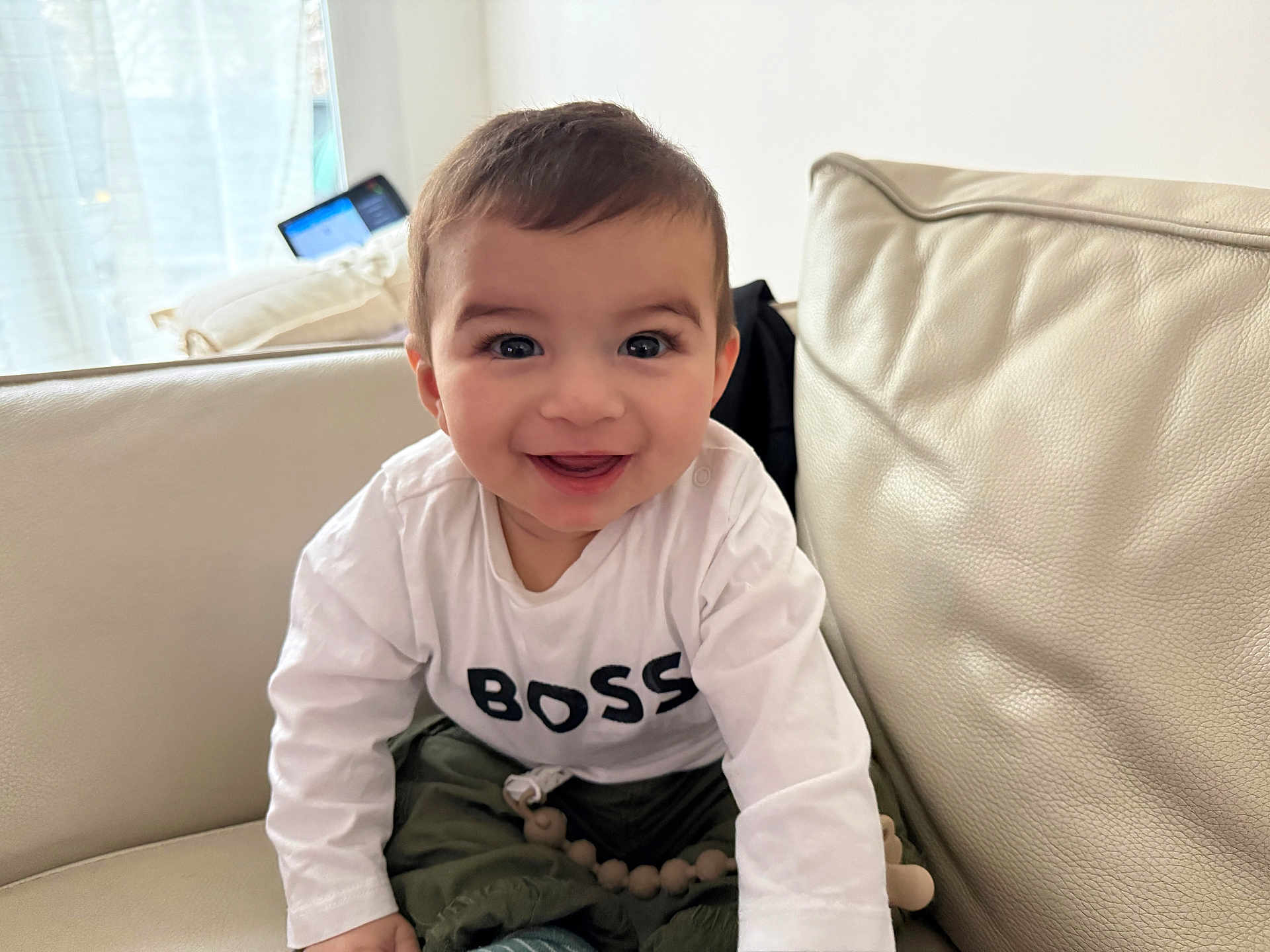 Qayim a rejoint le concours — aidez-le/la à gagner de superbes lots ! baby, child, infant, toddler, smiling, face, eyes, hair, white_shirt, text_on_shirt, couch, sofa, living_room, indoor, portrait, happy, sitting, pacifier_clip, cushions, adorable