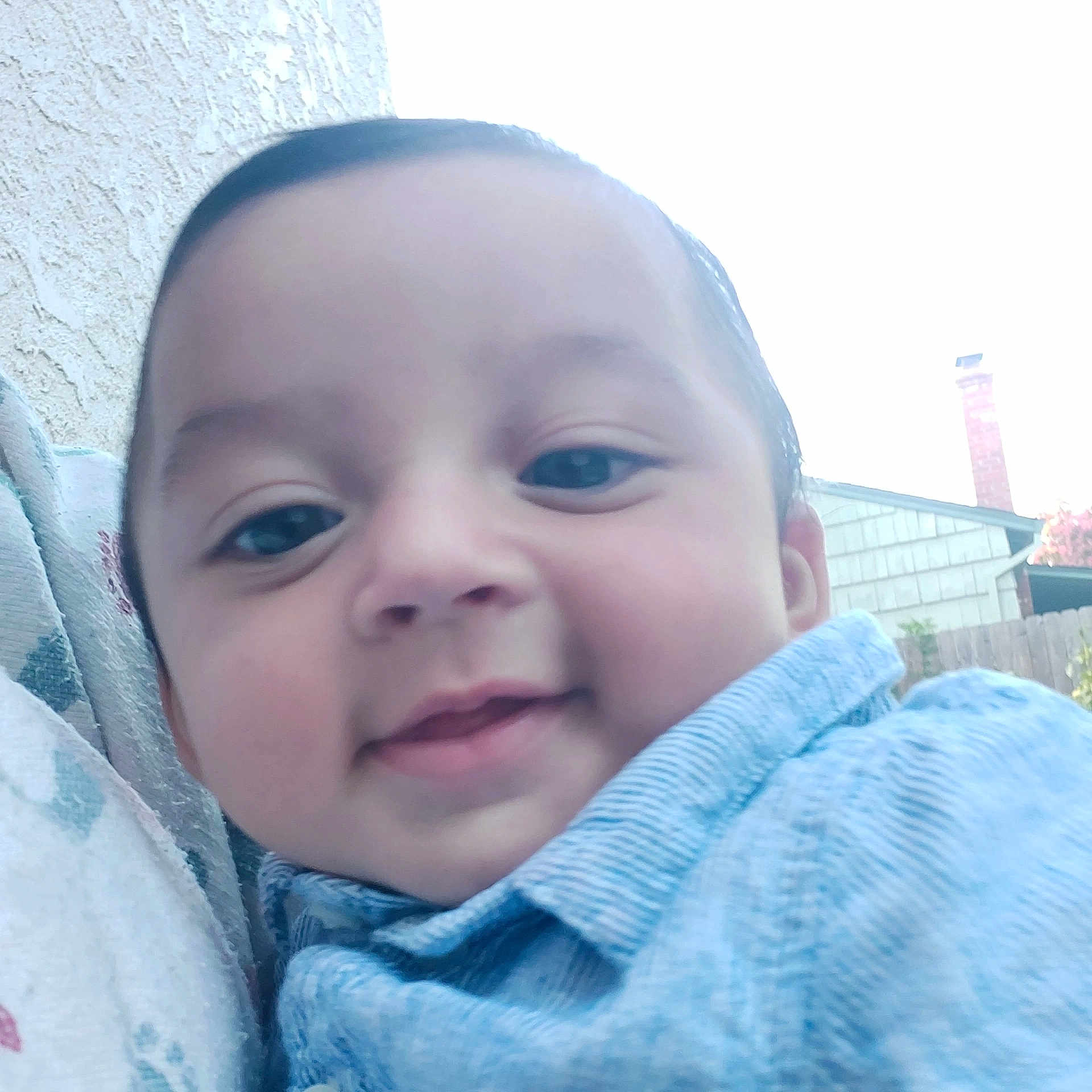 William is registered to the contest to win money with this photo: baby, baby_clothing, blue_shirt, casual, cheeks, child, closeup, daylight, face, fence, happy, head, house, infant, outdoor, person, portrait, skin, smile, young_child