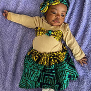 Lucimary a rejoint le concours — aidez-le/la à gagner de superbes lots ! baby, infant, child, headband, bow, skirt, patterned_fabric, purple_blanket, lying_down, portrait, cute, onesie, long_sleeve, hand, toes, gaze, cozy, textile, ruffled_waist, accessory